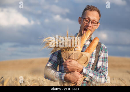 Homme affamé mord dans le champ de seigle baguettes. Banque D'Images