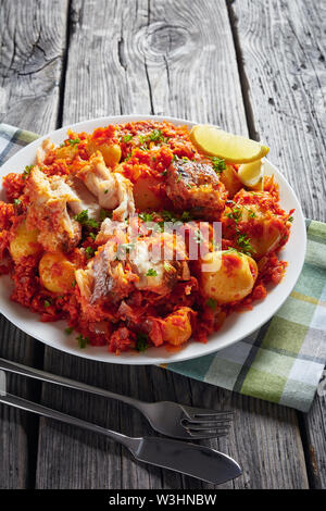 Close-up de merlu ragoût de poisson avec pommes de terre et de carotte oignon sauce tomate servi sur une plaque blanche avec des quartiers de citron, vertical Vue de dessus Banque D'Images