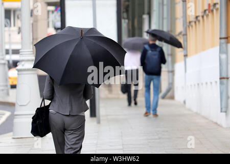 La pluie dans une ville, slim femme avec parapluie noir marche sur une rue, vue arrière. Les gens en temps de pluie, l'été ou l'automne storm Banque D'Images