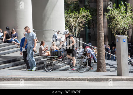 Location courier peddles montée dans le centre-ville de Sydney Bureau passé appréciant le déjeuner des travailleurs sur les mesures de No 1,Rue Bligh Sydney, Australie Banque D'Images