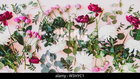 Différentes fleurs d'une télévision à jeter. Les pivoines, roses rose mauve, des chrysanthèmes blancs et verts rameaux avec feuilles sur fond rose pastel, vue du dessus Banque D'Images