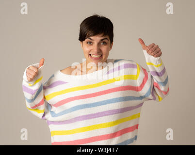 Portrait de heureux et surpris young caucasian female smiling and showing Thumbs up rayé multicolore en geste isolé de cavalier sur zone neutre Banque D'Images