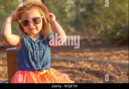 Une jolie petite fille blonde dans le parc. Elle est de porter un chapeau et des lunettes Banque D'Images