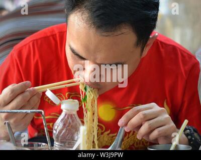 Homme d'âge moyen mange nouilles thaï jaune avec des baguettes. Banque D'Images