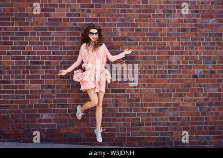 Jeune femme joyeuse s'amusant sauter contre un mur de briques Banque D'Images