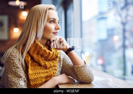 Jeune femme sérieuse à la recherche d'une fenêtre dans un café pendant la journée d'hiver Banque D'Images