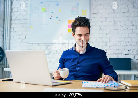 Happy young man working in creative office sur l'ordinateur portable à la recherche sur des documents Banque D'Images