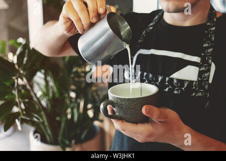 Lait fouetté barista pouring homme mousse de pitcher en tasse avec du café en café Banque D'Images