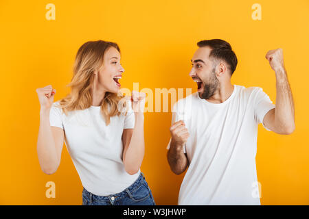 Portrait de couple heureux positive l'homme et de la femme dans les t-shirts se réjouir et work isolé sur fond jaune Banque D'Images
