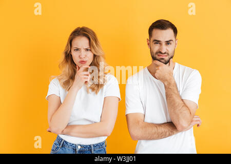 Image de l'homme et la femme couple irritée froncer et toucher le menton en regardant sur fond jaune isolé de l'appareil photo Banque D'Images