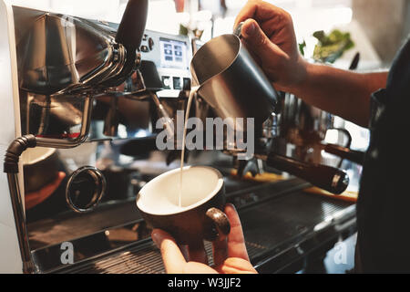 Lait fouetté barista pouring homme mousse de pitcher en tasse avec du café à proximité d'une machine à café professionnelle in cafe Banque D'Images