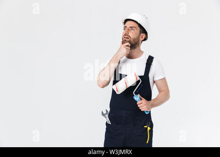 Portrait of a handsome builder barbu homme portant salopettes isolés sur fond blanc, tenant un pinceau Banque D'Images