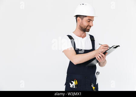 Certain constructeur barbu homme portant une combinaison et casque isolés sur fond blanc, de prendre des notes dans le bloc-notes Banque D'Images