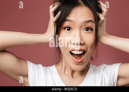 Portrait de l'étonnement des asian woman vêtus de vêtements de base et demande à la caméra à la tête durant l'obtention de plus de fond rouge isolé en studio Banque D'Images