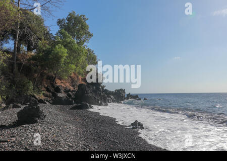 Plage de lave noire avec des cailloux et des pierres. Rocher de lave volcanique. Légèrement ondulé et la mer de l'eau mousseuse dans les vagues sur la côte. Banque D'Images