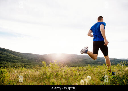 Retour homme runner s'exécutant sur le plateau d'été dans l'herbe motley coucher du soleil Banque D'Images