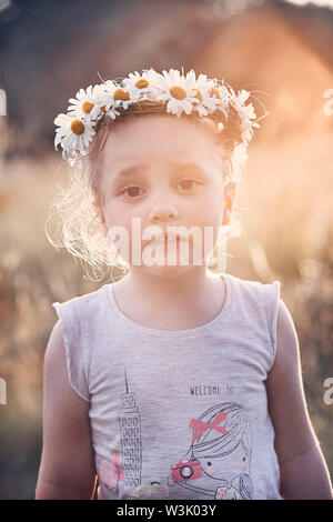 Petite fille portant une couronne de fleurs sauvages sur sa tête. Les gens sincères, vrais moments, situations authentiques Banque D'Images