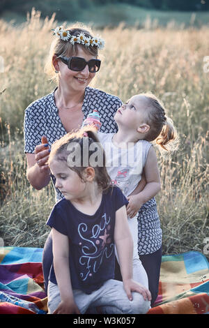 Famille de passer du temps ensemble sur un pré, près de la nature. Les parents et les enfants à jouer ensemble, faisant de couronne de fleurs sauvages. Les gens sincères, du vrai Banque D'Images