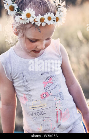 Petite fille portant une couronne de fleurs sauvages sur sa tête. Les gens sincères, vrais moments, situations authentiques Banque D'Images