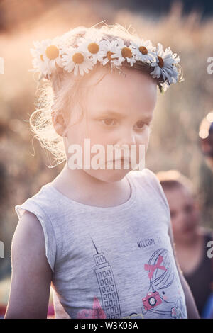 Petite fille portant une couronne de fleurs sauvages sur sa tête. Les gens sincères, vrais moments, situations authentiques Banque D'Images