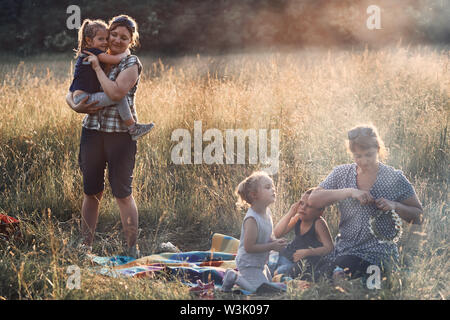 Famille de passer du temps ensemble sur un pré, près de la nature, les parents et enfants à jouer ensemble, faisant de couronne de fleurs sauvages. Les gens sincères, du vrai Banque D'Images