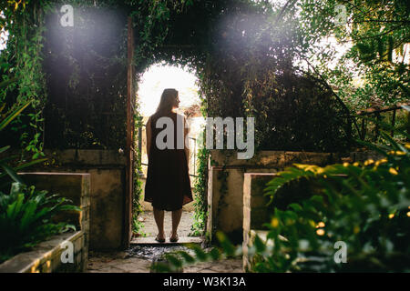 Femme debout dans un verdoyant entrée voûtée avec sun flare à la recherche sur le côté dans le jardin de la Concepcion Historical-Botanical, Malaga, Espagne Banque D'Images