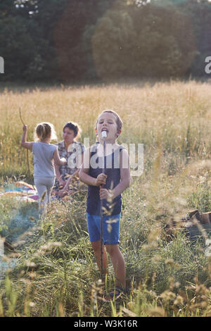 Boy eating une guimauve après la torréfaction il sur un feu de camp sur une prairie. Les gens sincères, vrais moments, situations authentiques Banque D'Images