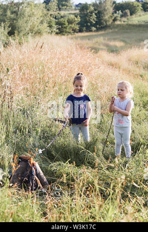 Petites filles guimauves grillées sur un feu de camp sur une prairie. Les gens sincères, vrais moments, situations authentiques Banque D'Images