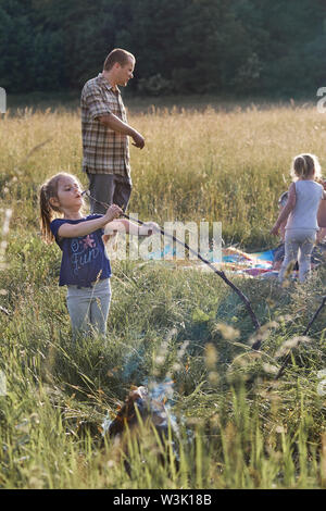 Little girl eating a après torréfaction guimauve il sur un feu de camp sur une prairie. Les gens sincères, vrais moments, situations authentiques Banque D'Images