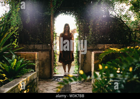 Jeune femme sérieuse debout dans une porte voûtée dans une serre face caméra avec les yeux fermés dans le Historical-Botanical La Concepcion Jardin, Ma Banque D'Images