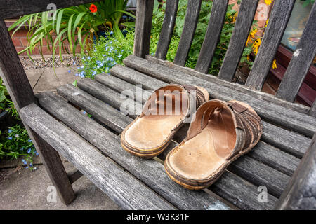 Une paire de sandales en cuir pour hommes sur un siège en bois dans un jardin. Banque D'Images