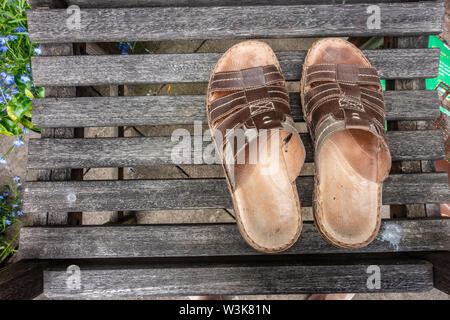 Une paire de sandales en cuir pour hommes sur un siège en bois dans un jardin. Banque D'Images