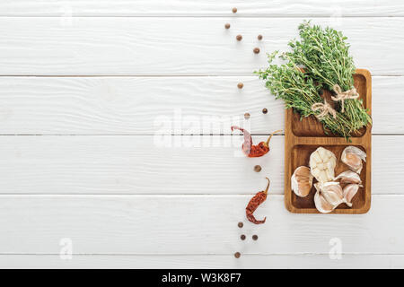 Vue de dessus de piments séchés, poivre noir près de board à l'ail et le thym sur table en bois blanc Banque D'Images