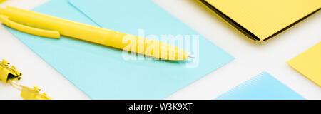 Vue panoramique tourné de dossier jaune, trombones et stylo sur enveloppe bleue sur fond blanc Banque D'Images