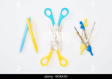 Vue de dessus de jaune et bleu ciseaux, stylos et des boussoles sur fond blanc Banque D'Images