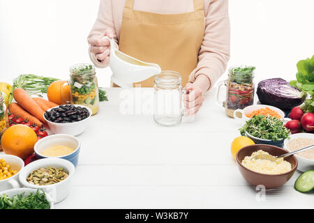 Portrait de femme en tablier d'ajouter de l'huile en verre vide sur la table en bois isolé sur blanc Banque D'Images