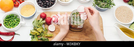 Portrait de femme en ajoutant des tranches de radis dans un pot avec de la salade sur le tableau blanc en bois tourné, vue panoramique Banque D'Images