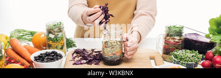 Portrait de femme en ajoutant de l'aire du chou rouge dans un bocal en verre sur la table en bois isolé sur blanc, vue panoramique tourné Banque D'Images