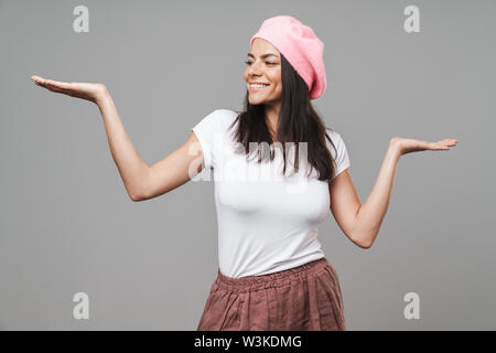 Gros plan Photo de jolie femme en t-shirt de base et beret smiling while jeter les armes sur fond gris isolé Banque D'Images