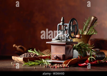 Ancien moulin à poivre avec des ustensiles de cuisine, épices et de romarin sur une table en bois. Banque D'Images