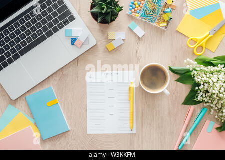 Vue du haut de la liste hebdomadaire, tasse de café, papeterie, ordinateur portable et de fleurs sur table en bois Banque D'Images