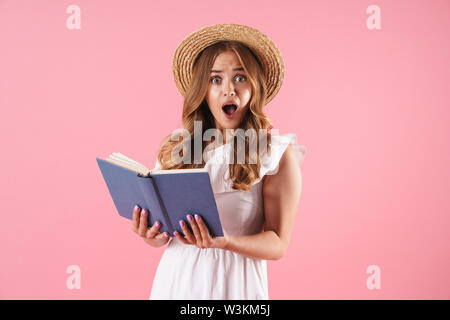 Image d'un choqué confus cute young Pretty woman posing isolé sur fond mur rose livre de lecture. À la caméra. Banque D'Images