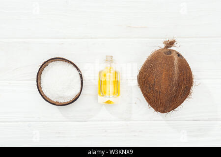 Mise à plat avec l'huile de noix de coco en bouteille, ensemble de la noix de coco et la moitié de la surface en bois blanc Banque D'Images
