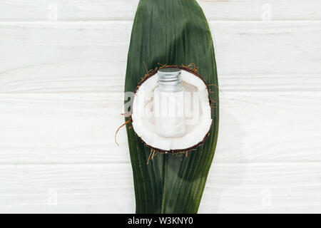 Vue de dessus du produit de beauté noix de coco en bouteille sur la moitié de la noix de coco et palme verte sur la surface en bois blanc Banque D'Images