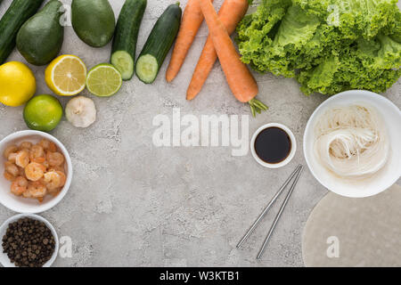 Vue de dessus de citrons, limes, avocats, carottes, le poivre noir, les crevettes, la sauce soja, papier de riz, l'ail,les nouilles et laitue sur tableau Banque D'Images