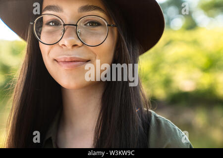 Photo de jeune femme aux longs cheveux noirs portant des lunettes et chapeau élégant balade dans Green Park, journée ensoleillée Banque D'Images