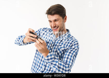 Photo de heureux l'homme à chemise décontractée jouer jeu vidéo sur téléphone cellulaire isolé sur fond blanc Banque D'Images