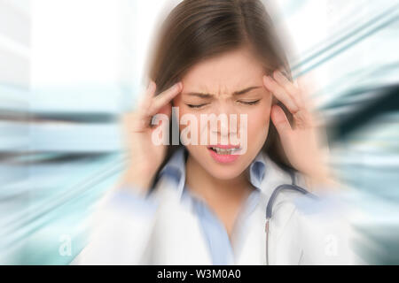 Migraine et maux de tête - médecin a souligné. Femme médecin / Infirmière avec migraine surchargés et stressés. Professionnel de la santé in lab coat wearing stethoscope à l'hôpital. Banque D'Images