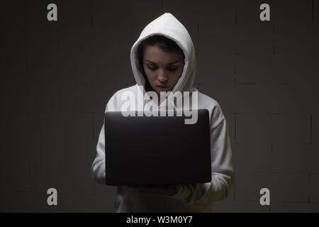 Une femme dans un capot est à l'aide d'un ordinateur portable. Hacker est à l'aide d'un ordinateur portable. Banque D'Images