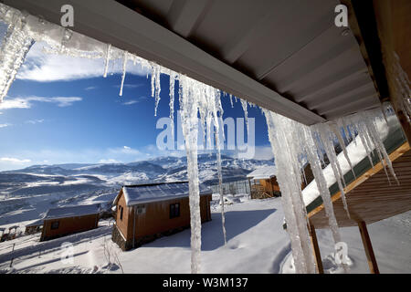 Pavillon avec grand soleil, les glaçons et les petites maisons en bois à l'hiver enneigé des montagnes. Montagnes du Caucase, l'Azerbaïdjan, Shahdagh. Vue grand angle. Banque D'Images